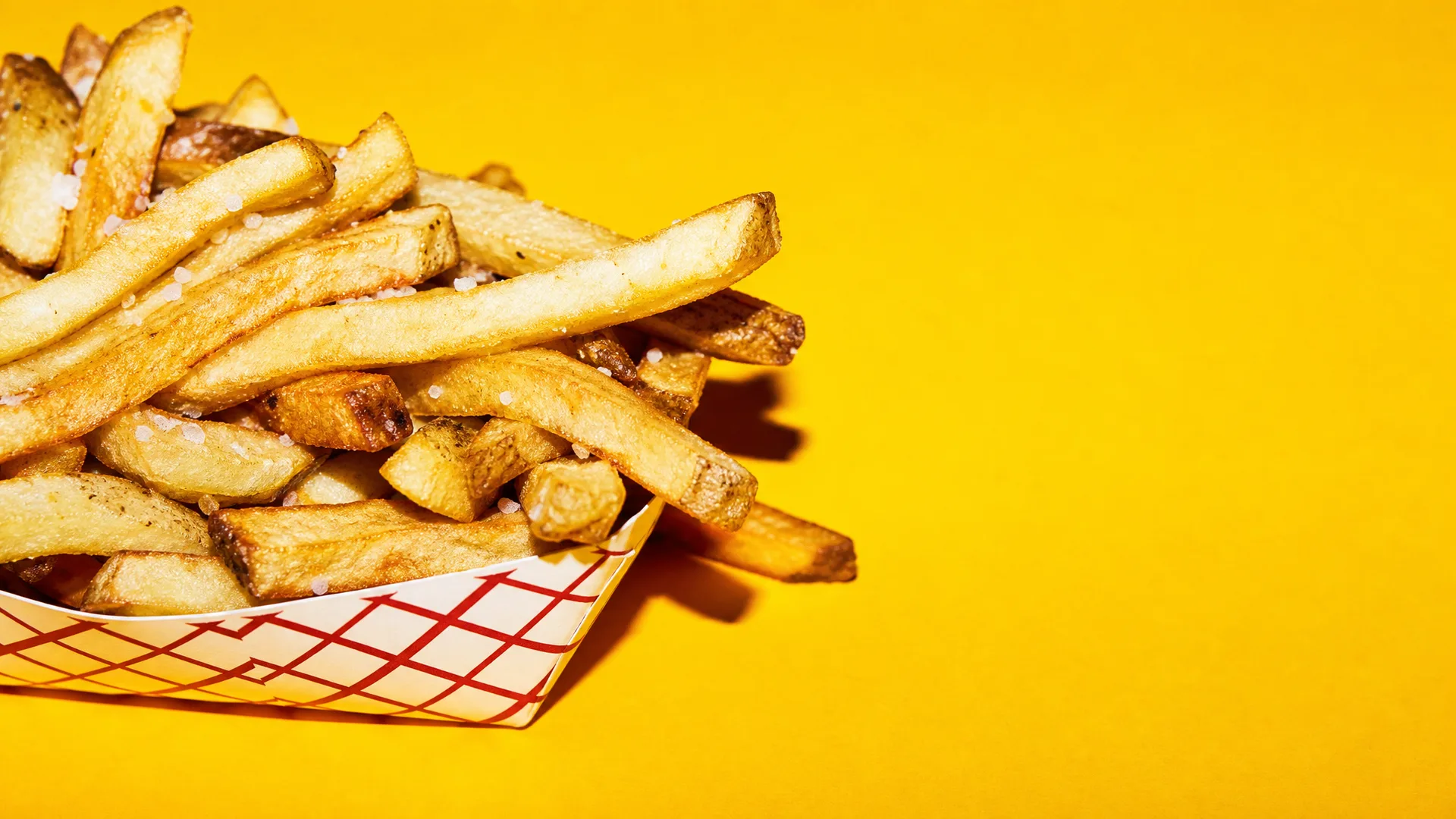 Frites qui débordent d'une barquette sur fond jaune